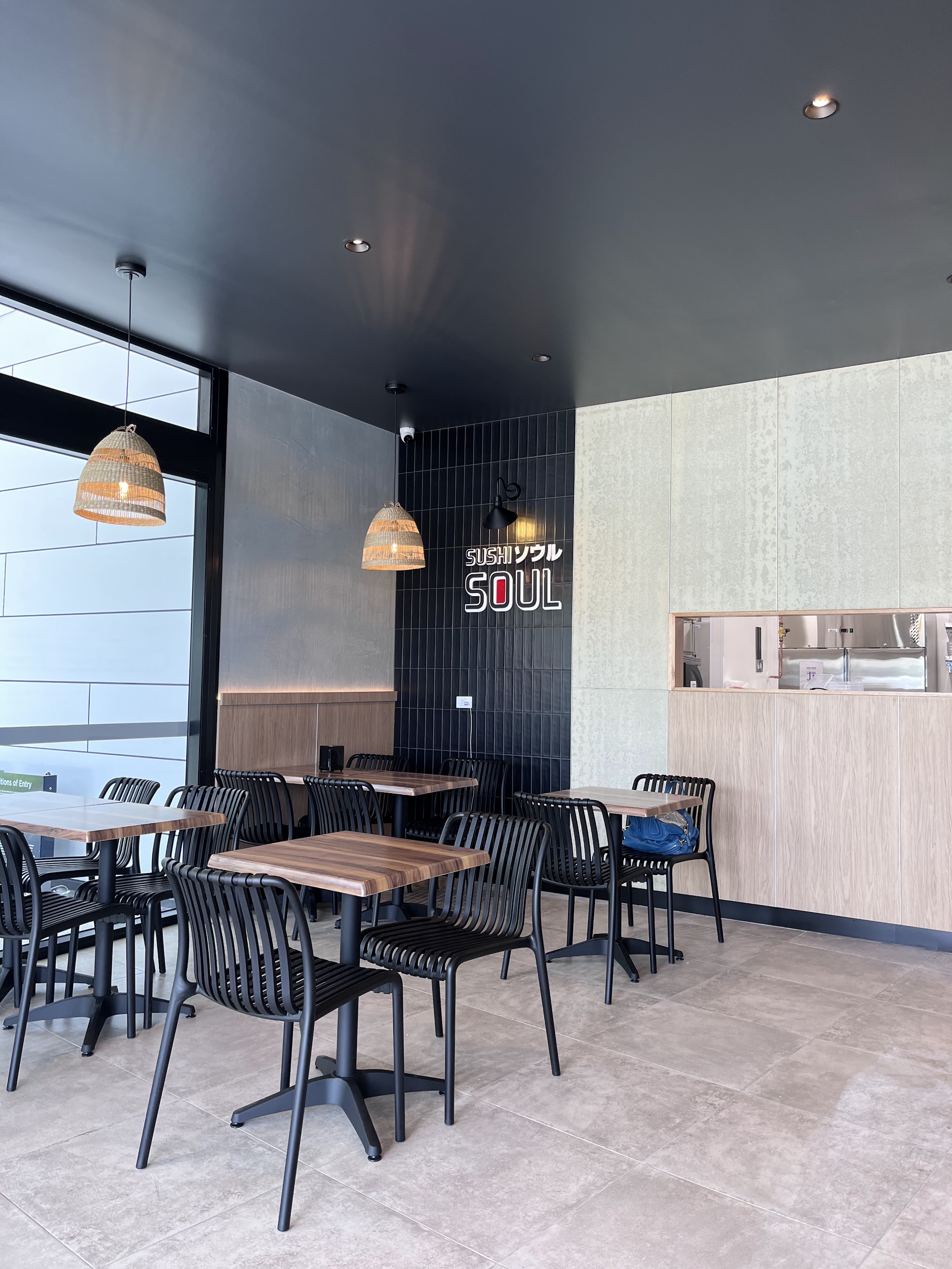 Inside Sushi Soul: timber tables, black chairs, rattan pendant lights and the Sushi Soul sign on a black tiled wall