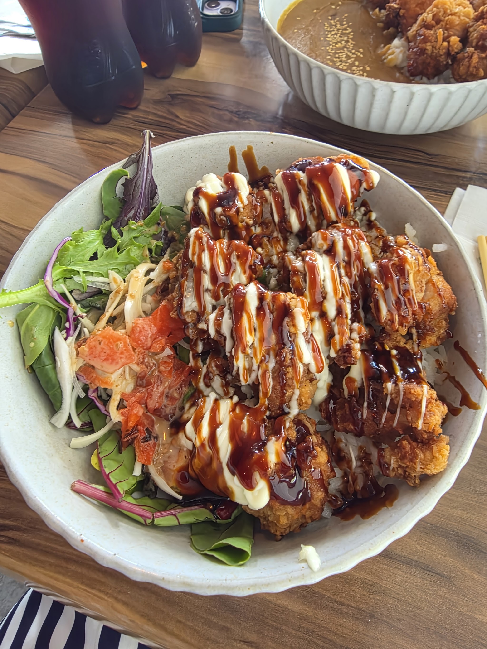 Karaage bowl with a side salad and mayo drizzle, with a curry bowl behind